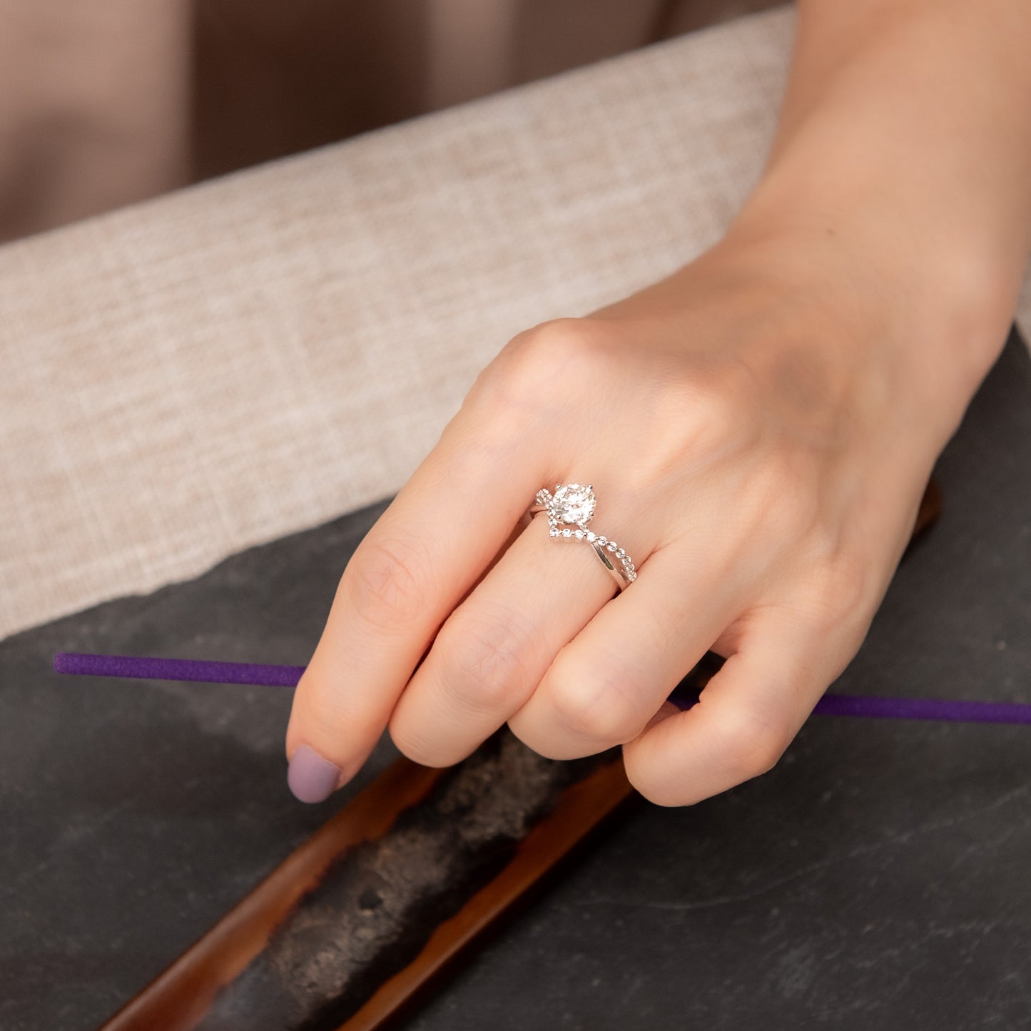 Hand wearing a silver ring with a diamond on a dark surface