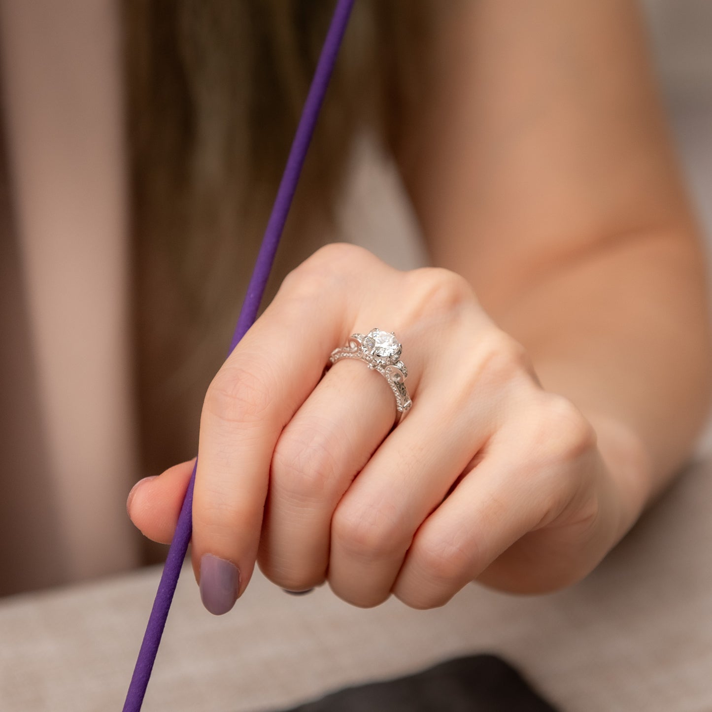 Hand holding a purple cord with a diamond ring on a neutral background