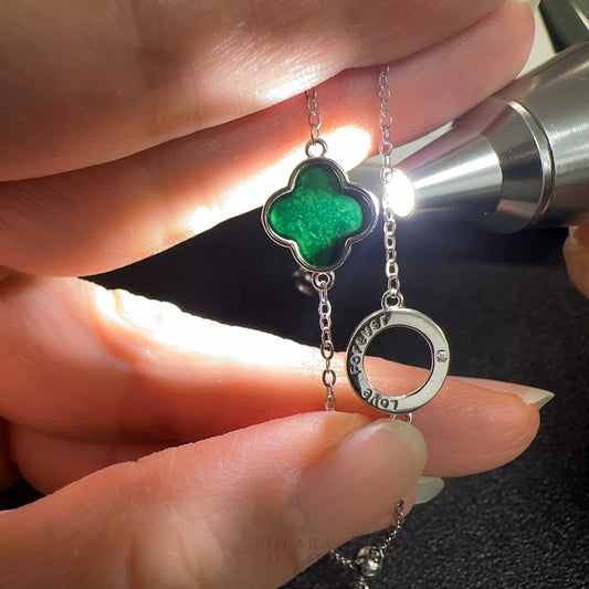 Close-up of a hand holding a necklace with a green pendant and silver ring, using a flashlight.