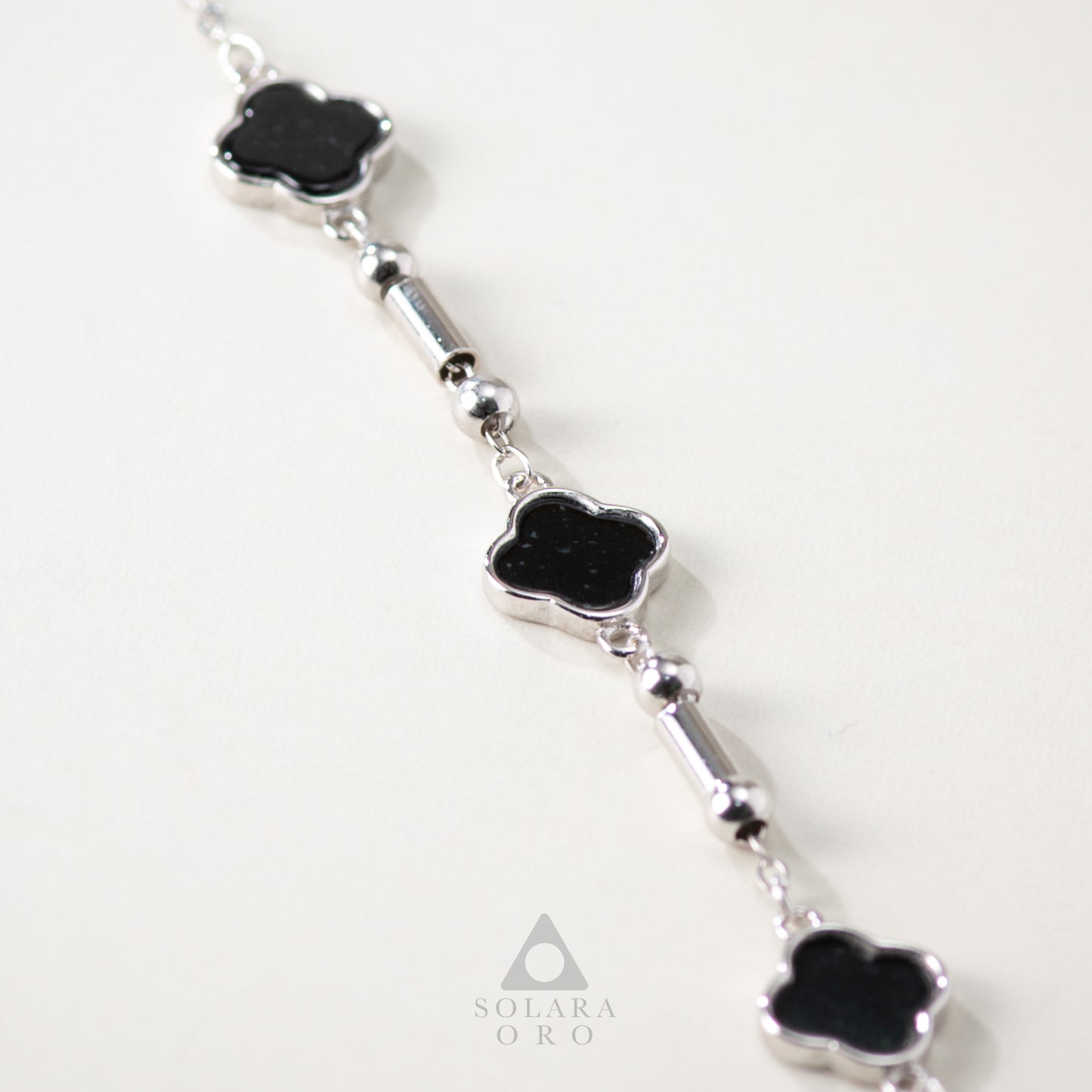 Silver bracelet with black clover-shaped stones on a white background, featuring the brand 'Soleara Oro'.