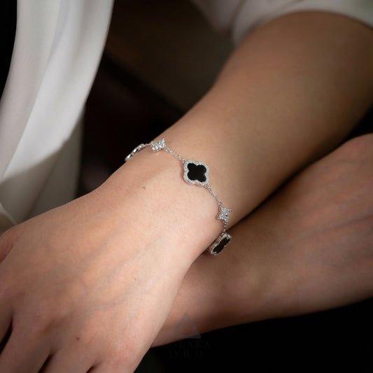 Close-up of a wrist wearing a delicate bracelet with a clover-shaped clasp.