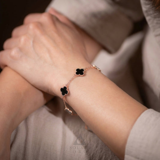 Rose gold bracelet with black clover charms on a wrist against a neutral background