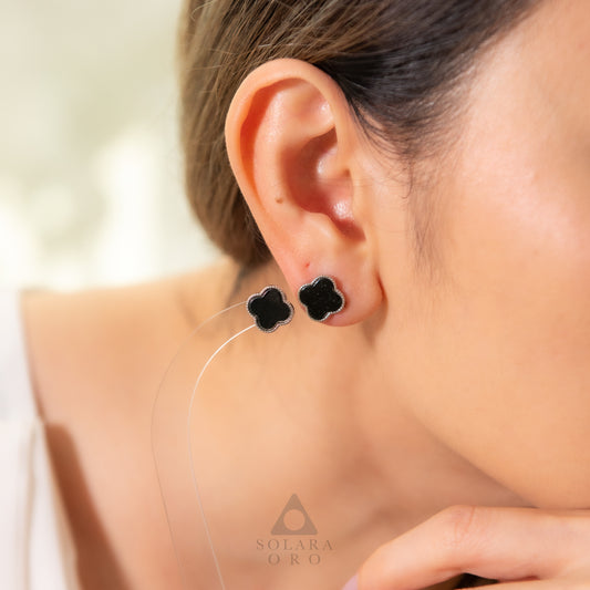 Close-up of a person wearing black clover-shaped earrings with a blurred background.