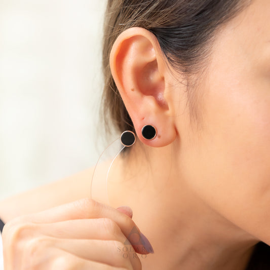 Close-up of an ear wearing black round earrings with a blurred background