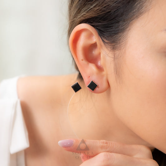 Close-up of a person wearing black square earrings with a blurred background