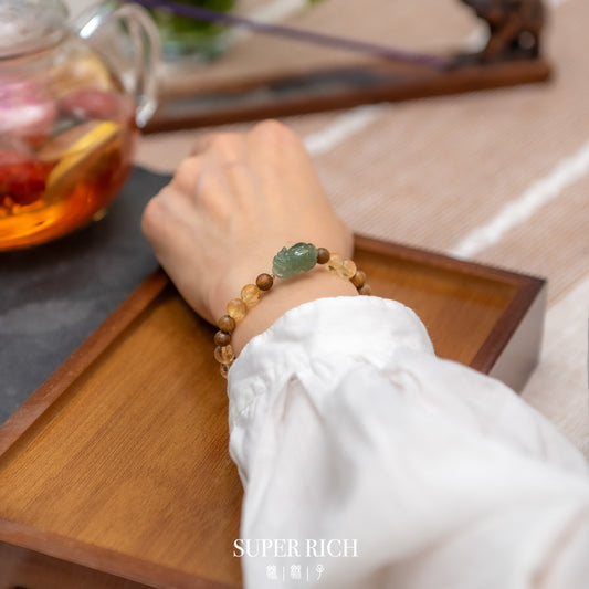 Person wearing a beaded bracelet with a green stone on a wooden tray with tea.