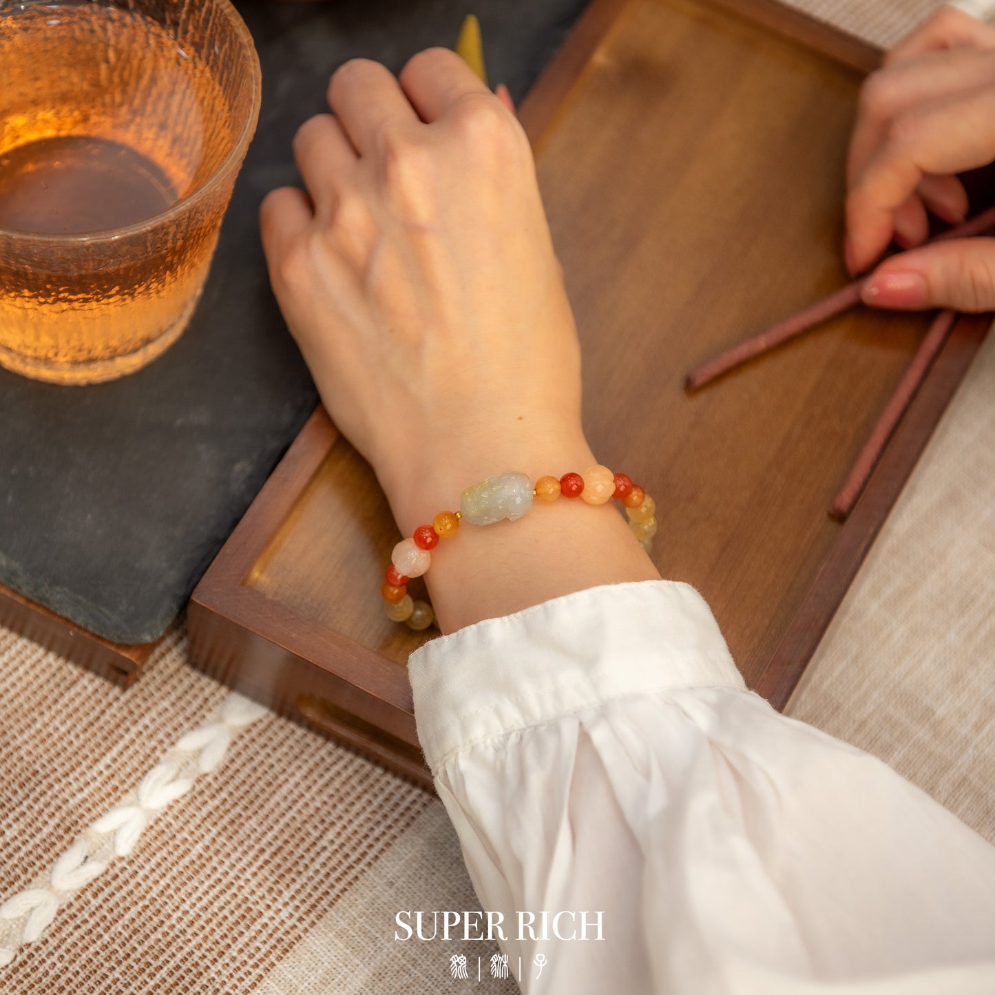 Person wearing a colorful beaded bracelet on a wooden table with a glass of tea.