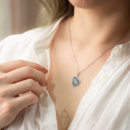 Person wearing a silver necklace with a heart-shaped pendant on a blurred background