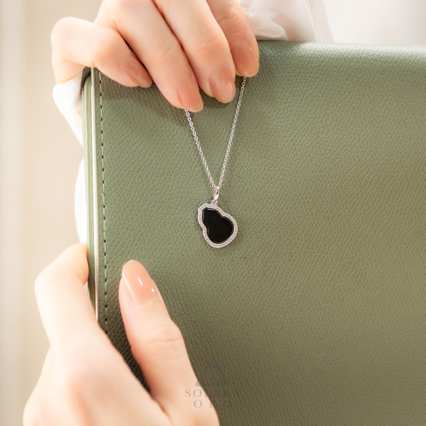 Necklace with a heart-shaped pendant held by hands against a green background