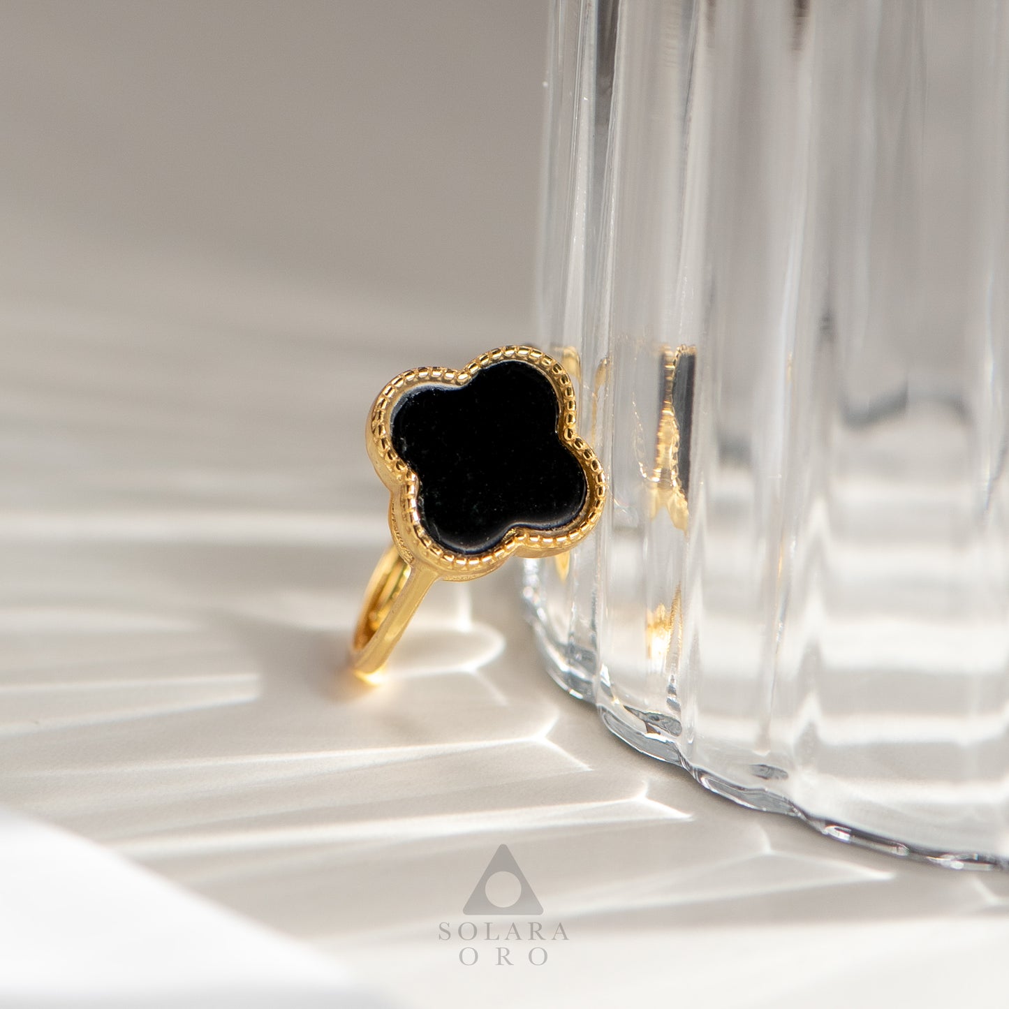 Gold ring with black stone on a glass surface, brand 'Soleria Oro' visible