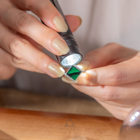Person using a flashlight to inspect a diamond ring with a visible brand logo.