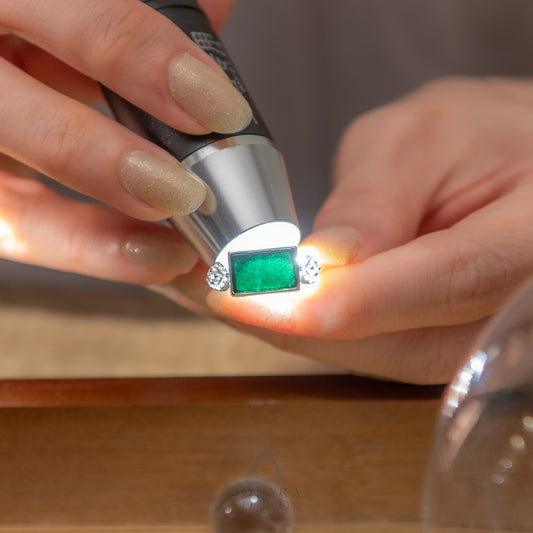 Person using a flashlight to inspect a green gemstone on a wooden surface.