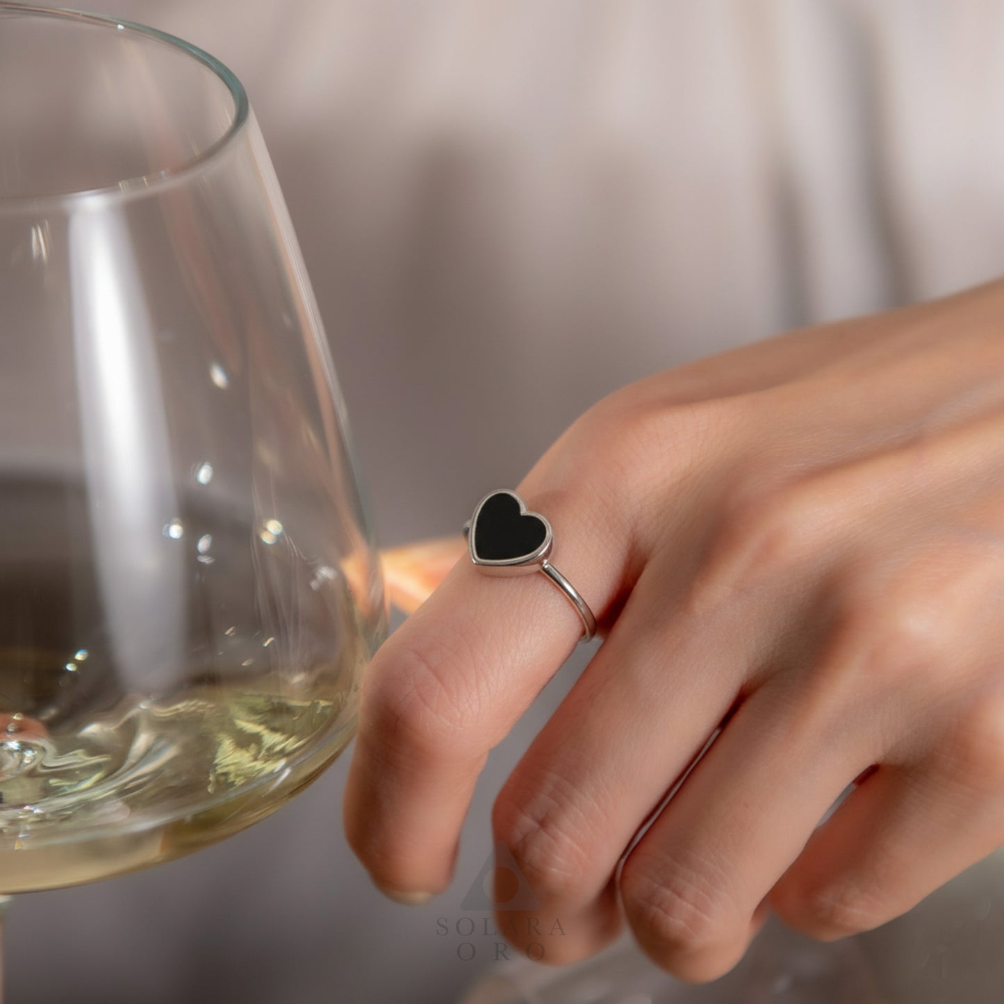 Hand wearing a black heart-shaped ring holding a glass of white wine.