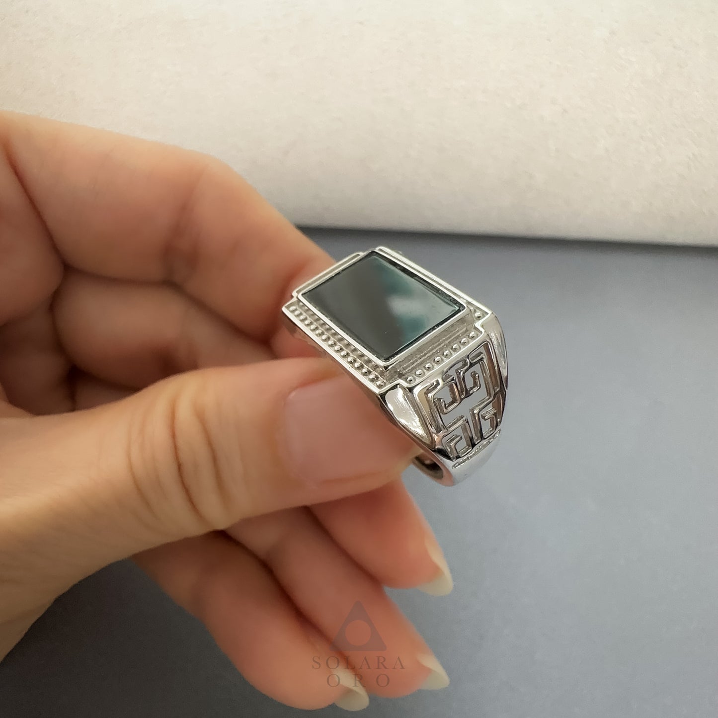 Silver ring with a dark stone held in a hand against a neutral background