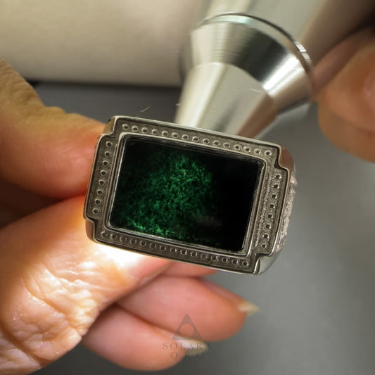 Silver ring with a green stone held by a hand against a neutral background