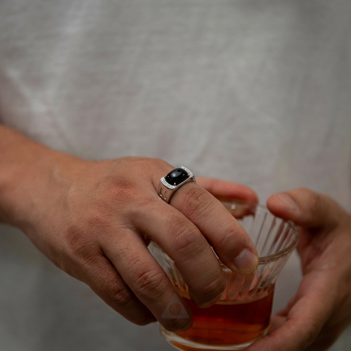 Hand holding a glass of amber liquid with a dark ring on a plain background