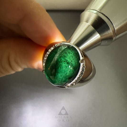 Green gemstone ring with silver band held by a hand against a neutral background, featuring the Solara Oro logo.