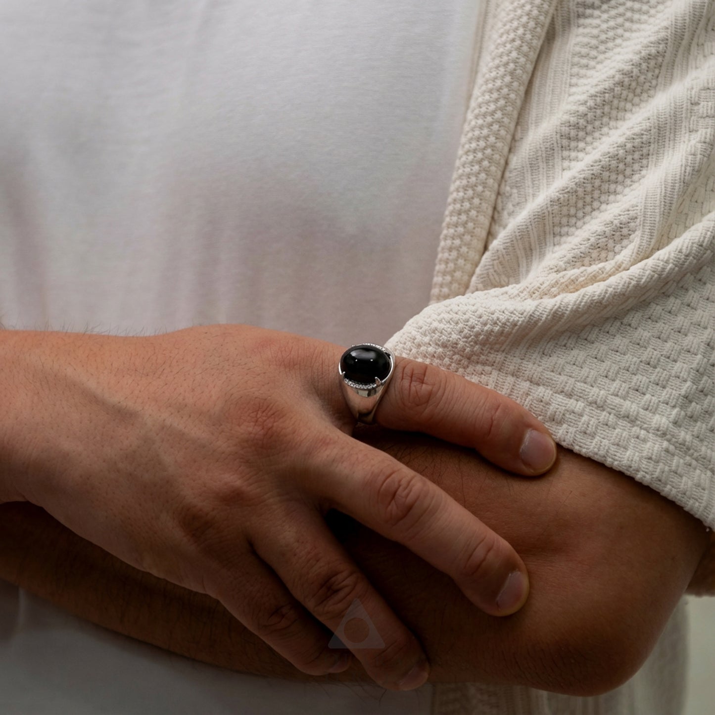 Hand wearing a ring with a black stone on a neutral background