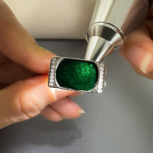 Ring with green stone held by a hand, close-up on a neutral background