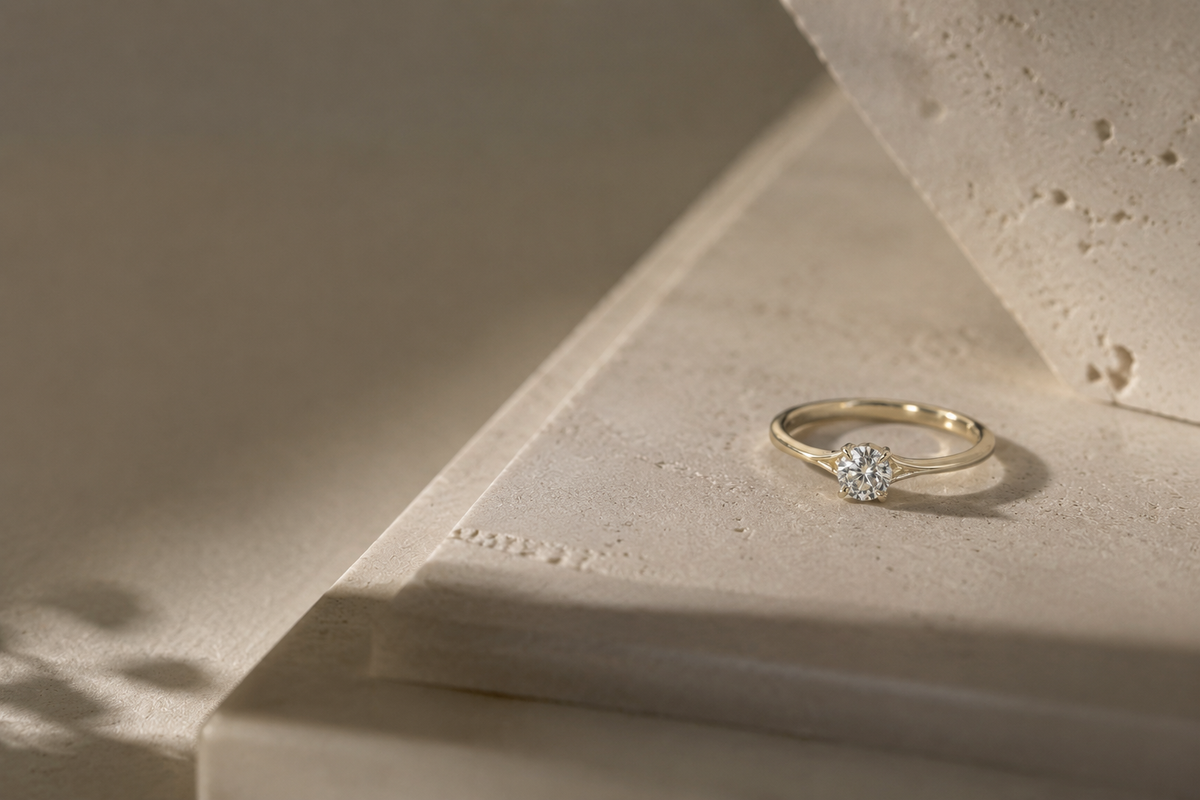 Yellow gold round solitaire diamond ring resting on a sunlit stone ledge with leaf shadows