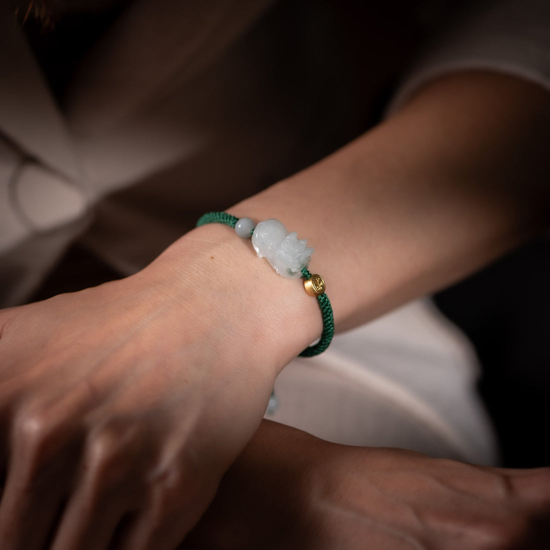 Person wearing a jade Pixiu bracelet with green cord, styled in a calm, modern setting to represent intention, balance, and refined everyday jewelry.