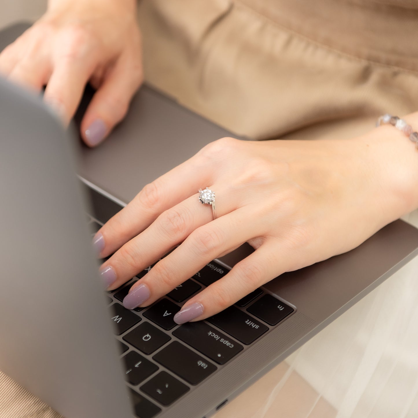 Close-up of hands typing on a laptop with a ring on one finger.