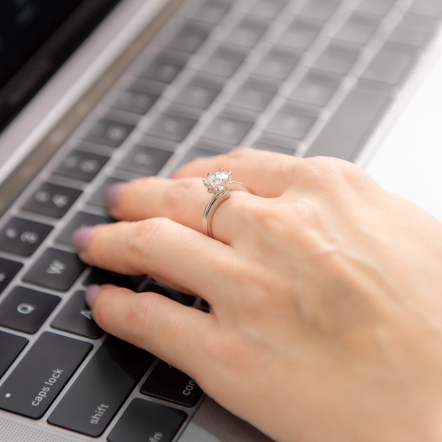 Hand with a ring typing on a laptop keyboard