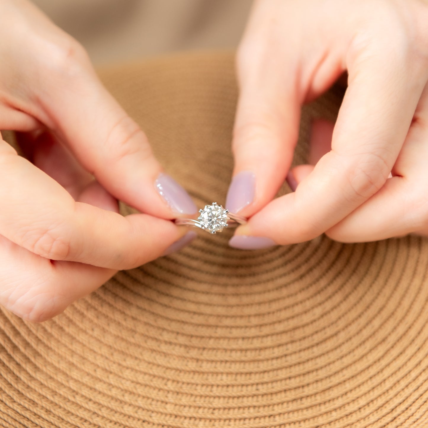Close-up of hands holding a diamond ring on a beige background