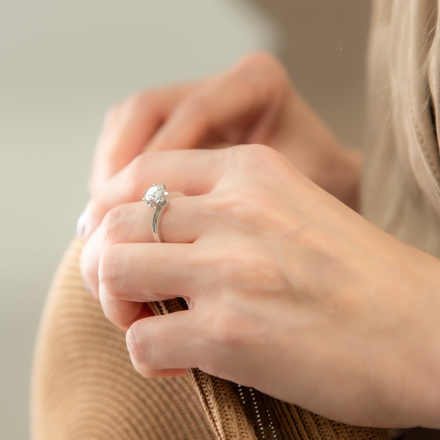 Close-up of a hand wearing a diamond ring on a neutral background