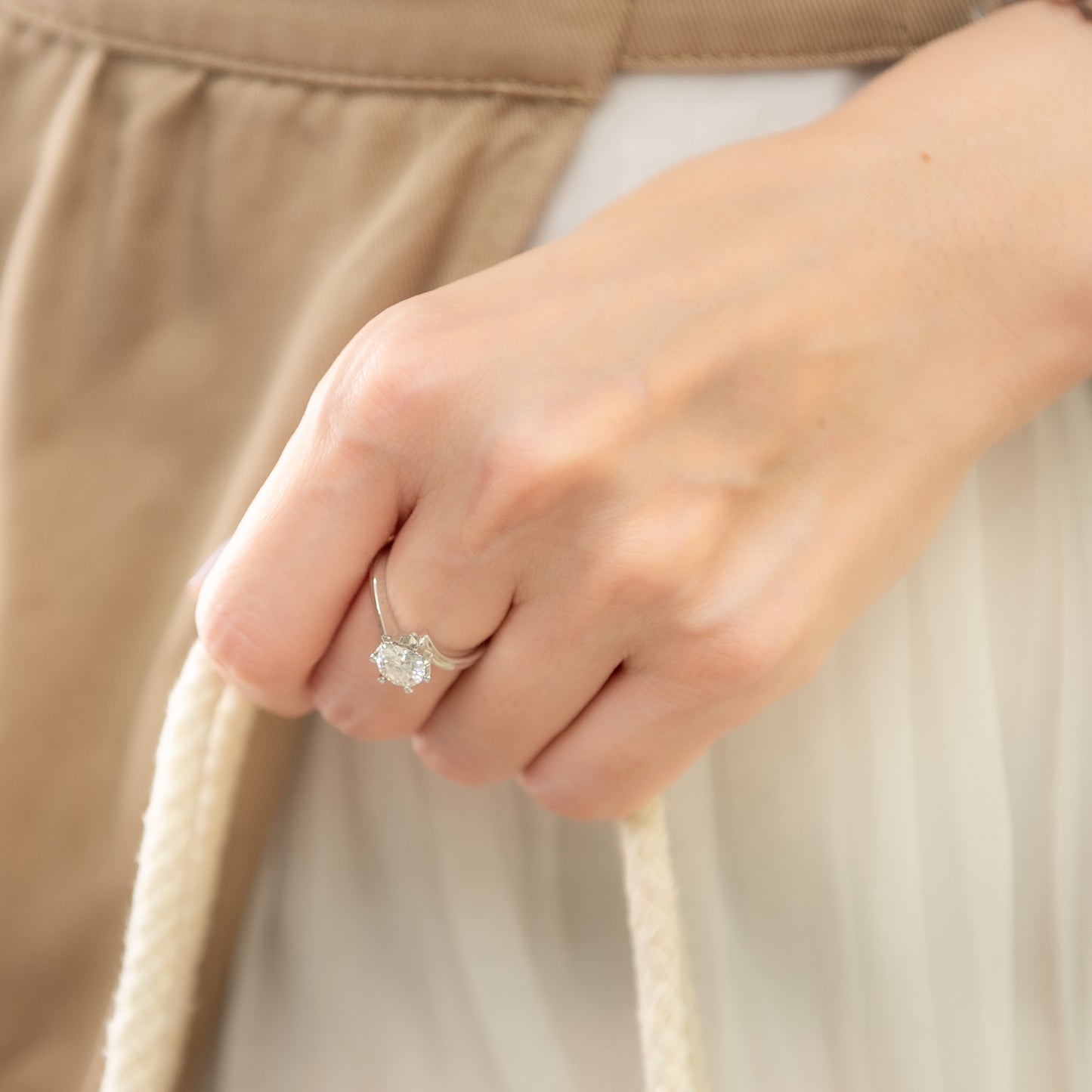 Close-up of a hand wearing a diamond ring with a neutral background