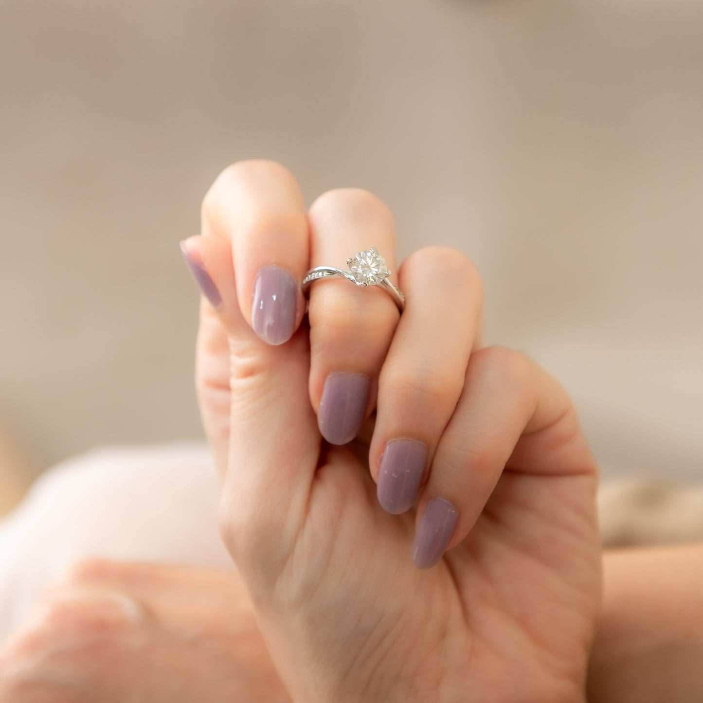Hand with purple nail polish wearing a silver ring with a diamond on a blurred background