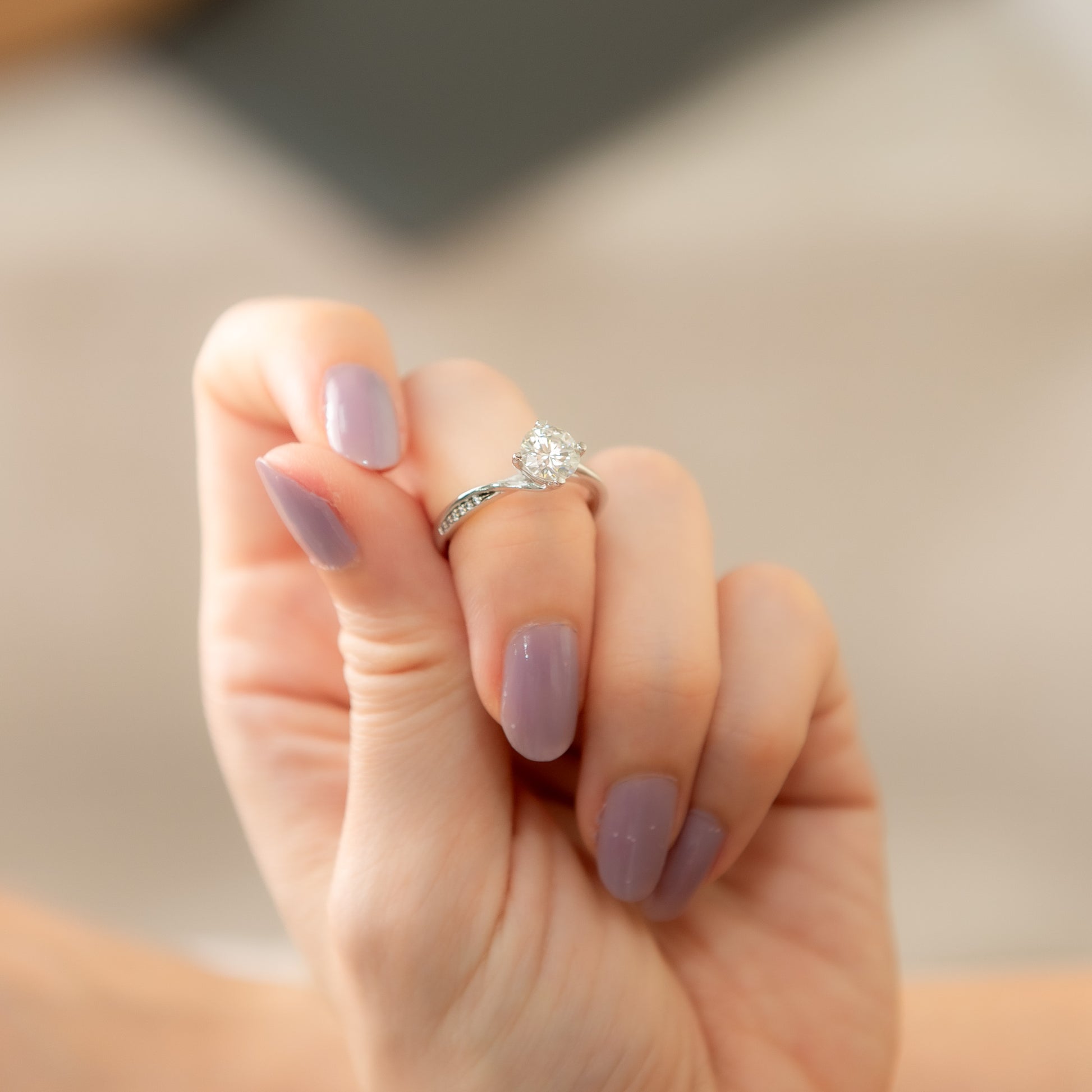 Hand with purple nail polish wearing a diamond ring on a neutral background