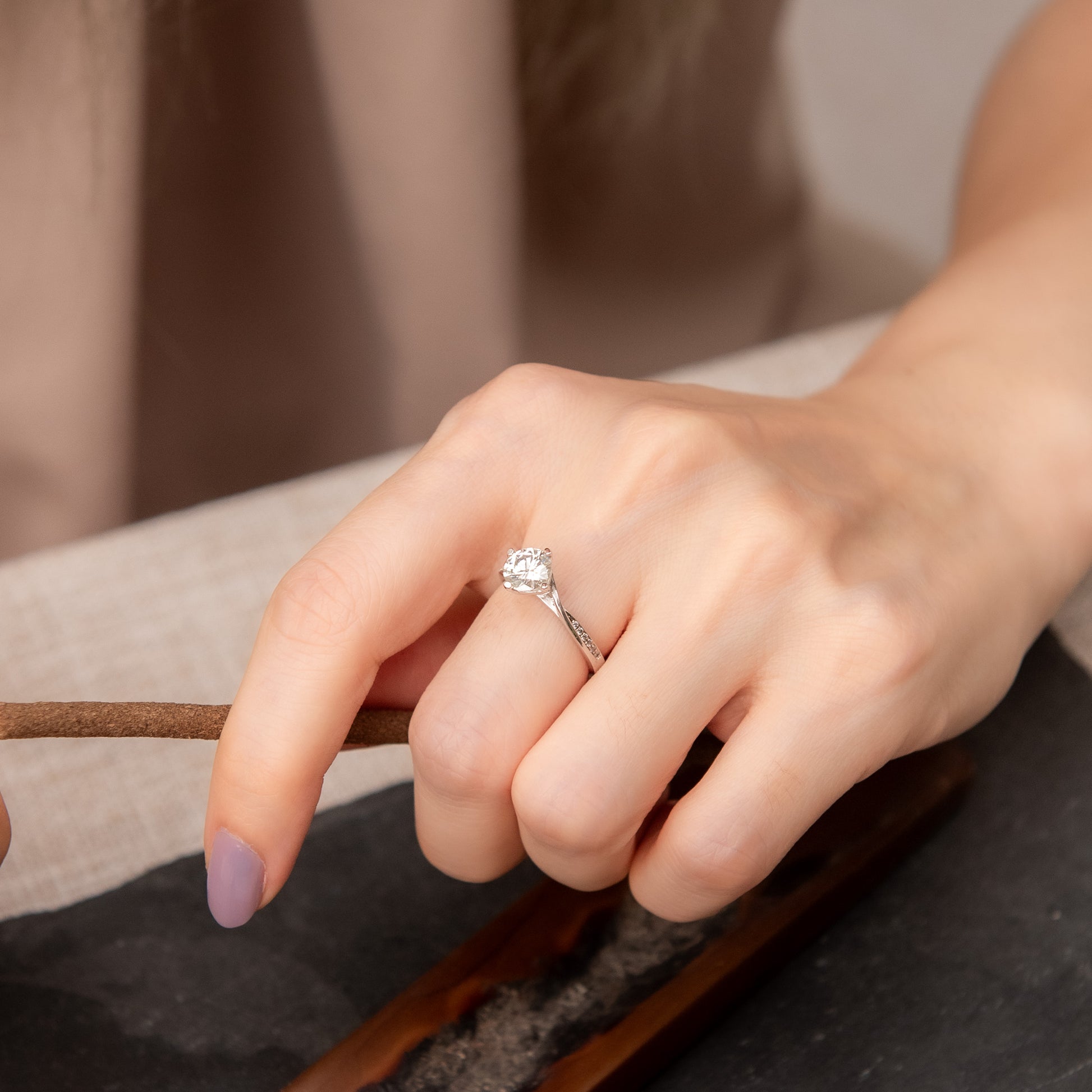 Hand wearing a diamond ring on a neutral background