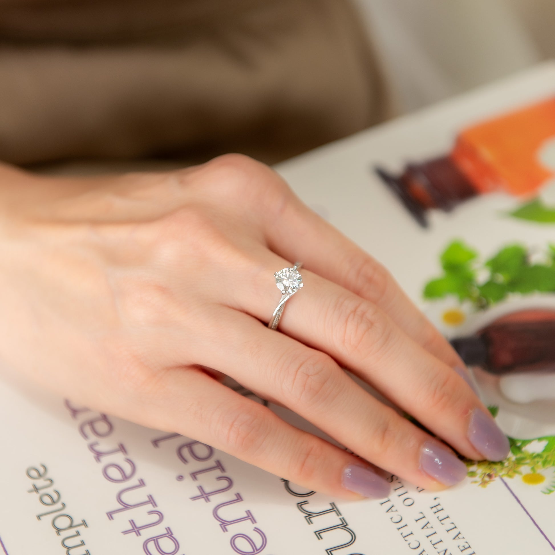 Hand wearing a silver ring with a diamond on a magazine page
