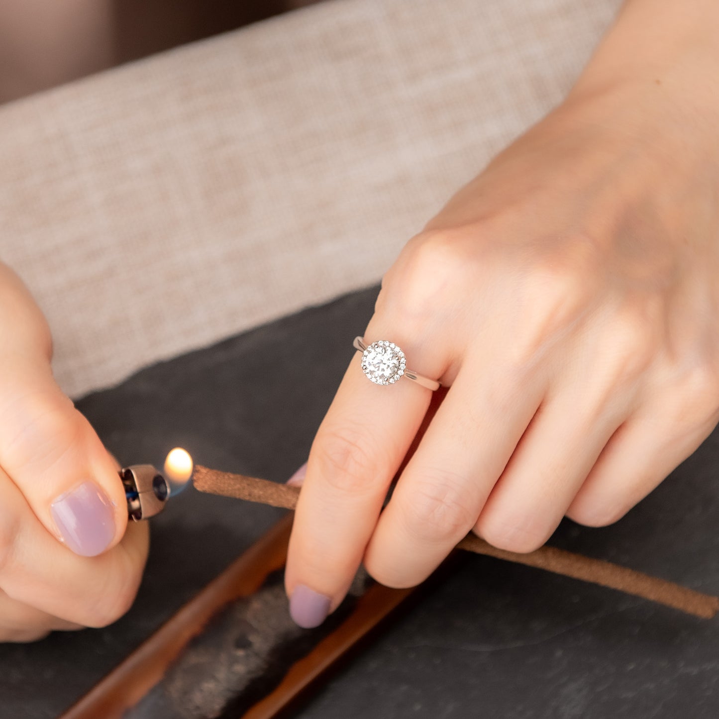 Person lighting a match with a lit matchbox, wearing a diamond ring.