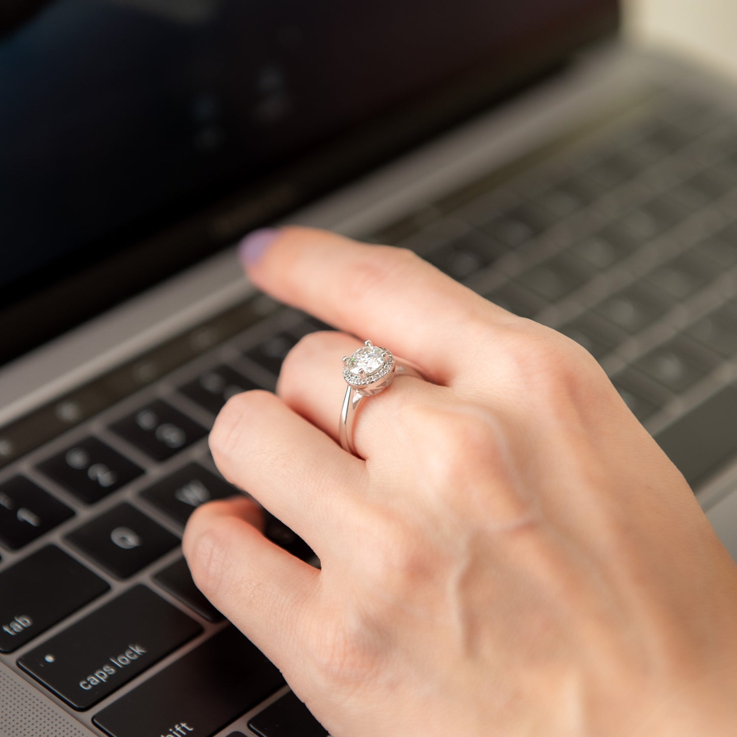 Hand typing on a laptop with a diamond ring on the finger