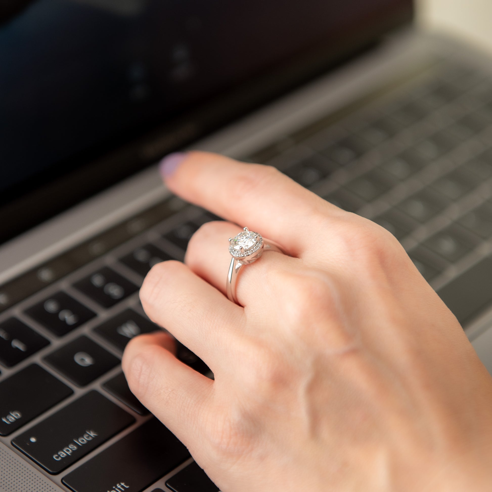 Hand typing on a laptop with a diamond ring on the finger