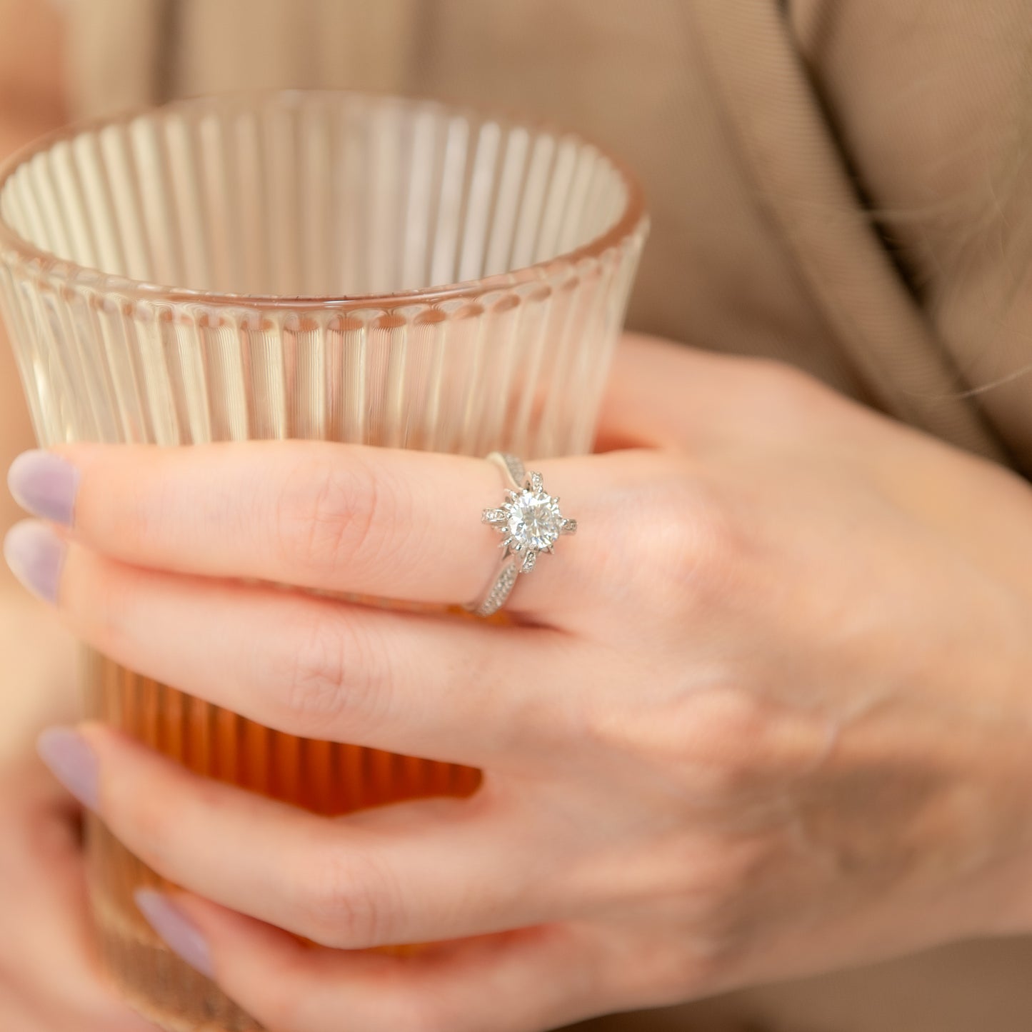 Person holding a clear glass cup with a diamond ring on a blurred background