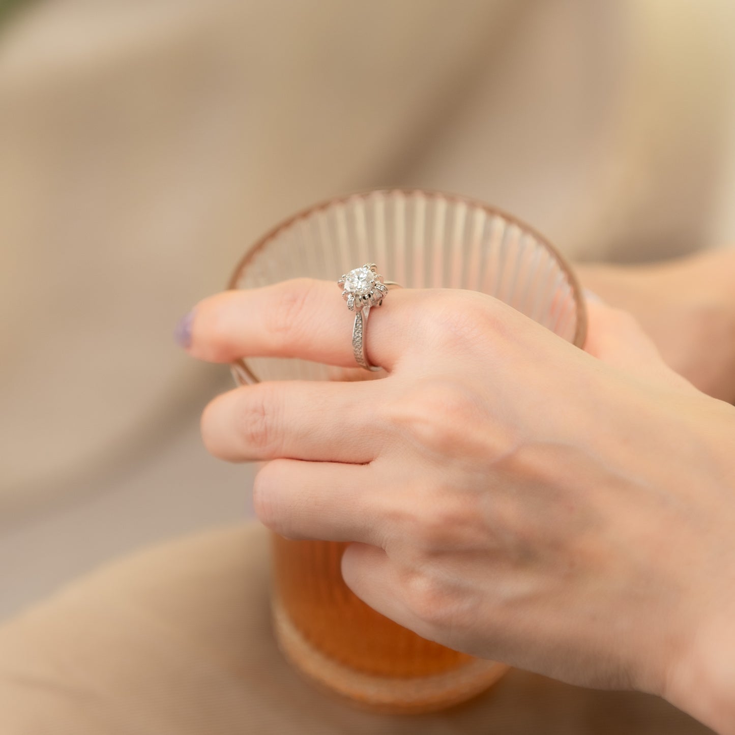Hand wearing a diamond ring holding a glass of orange juice.