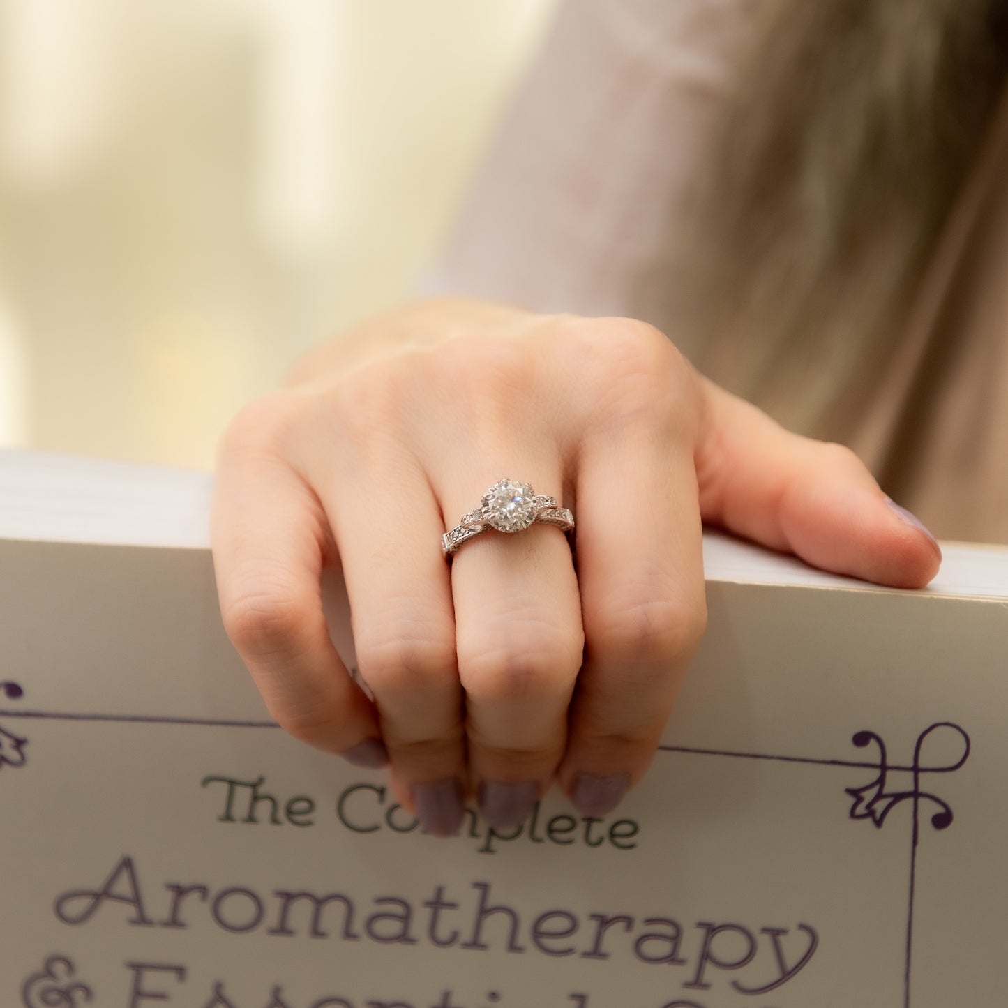 Hand wearing a diamond ring on a book titled 'The Complete Aromatherapy & Essential Oils'.