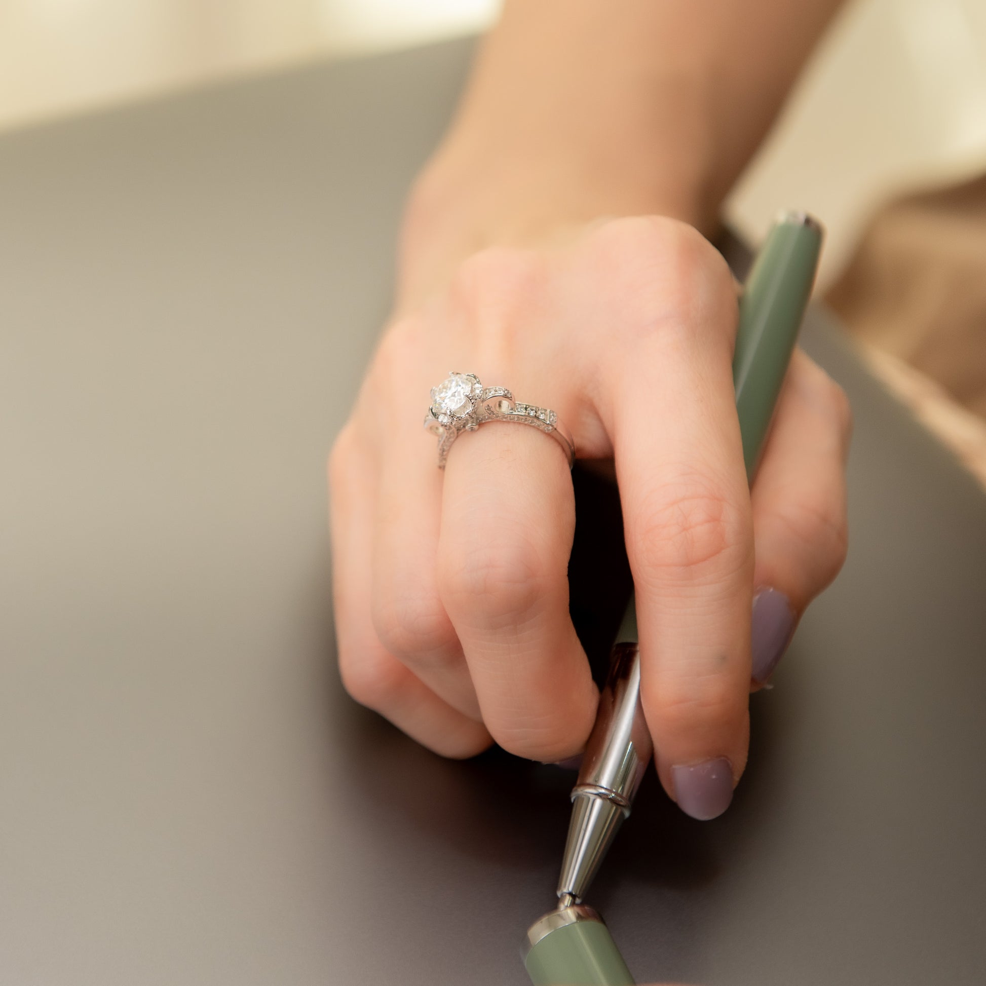 Hand holding a green pen with a diamond ring on a neutral background