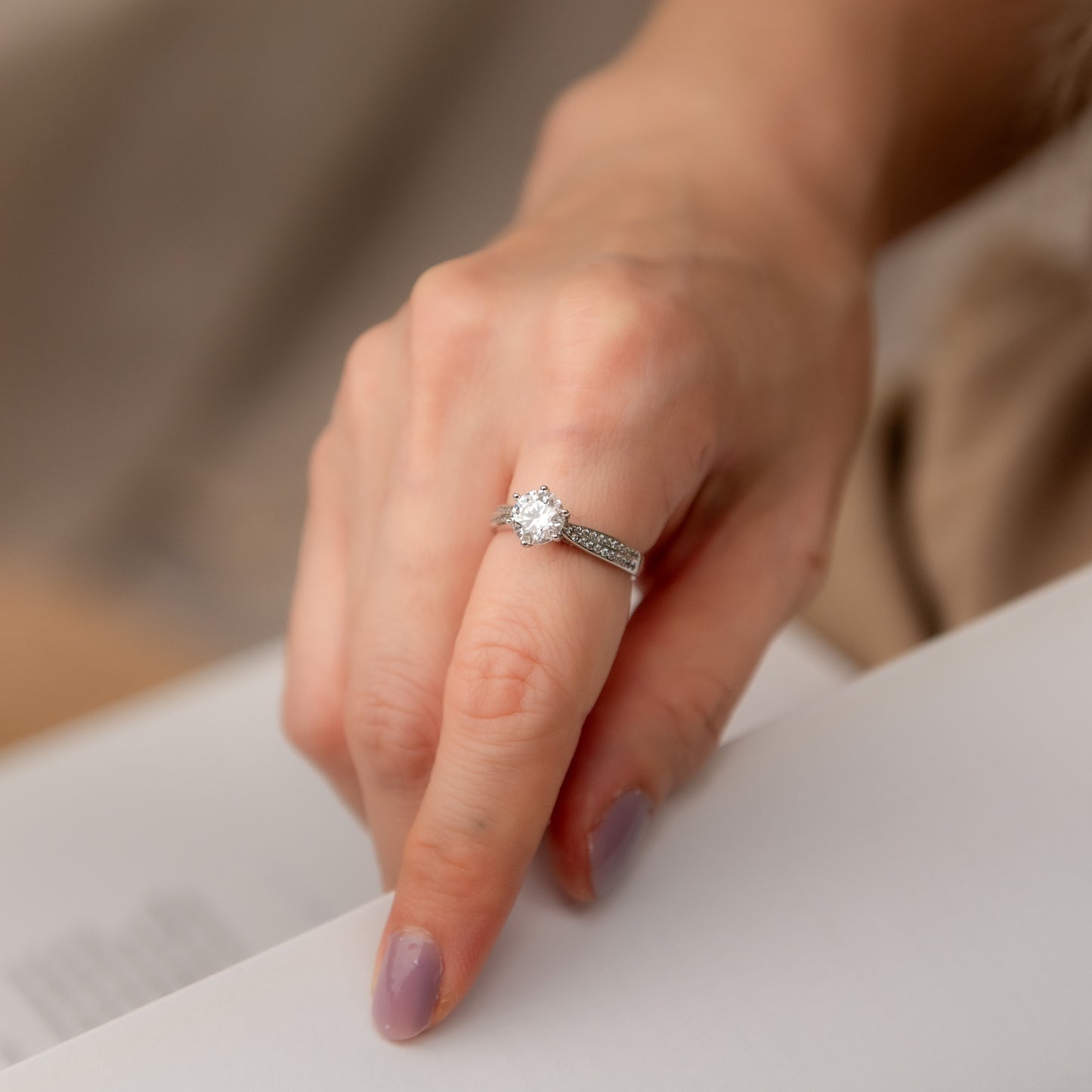 Close-up of a hand wearing a diamond ring on a neutral background