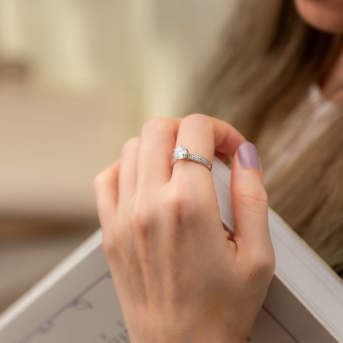 Hand wearing a diamond ring with a blurred background