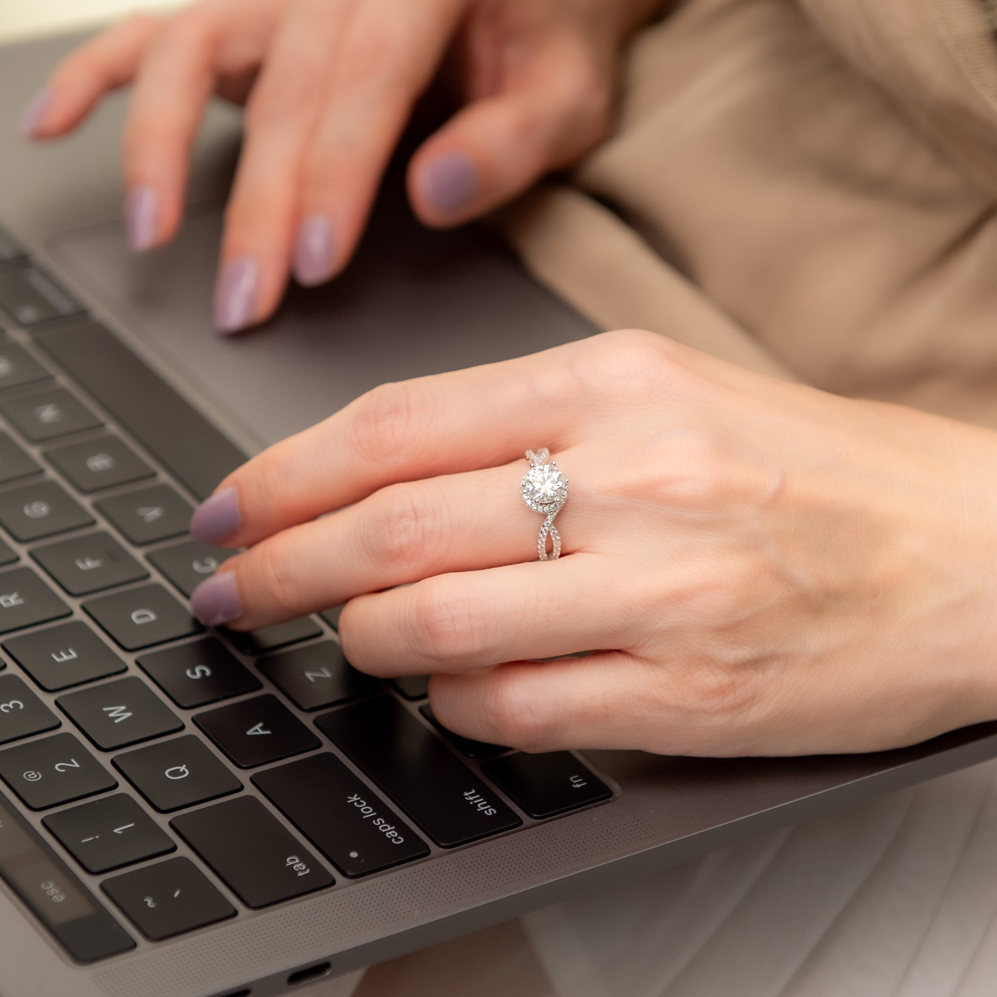Close-up of hands typing on a laptop with a diamond ring on the left hand.