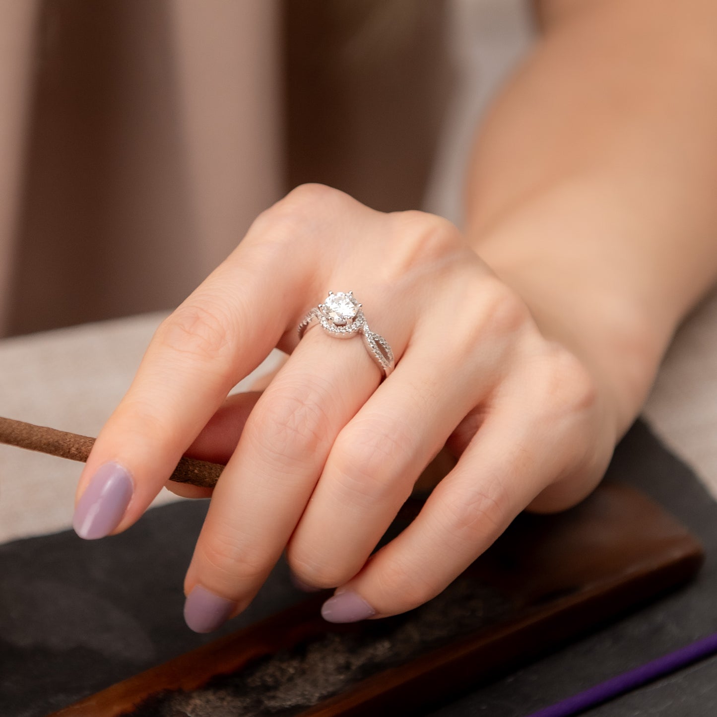Hand wearing a silver ring with a diamond, holding a stick with a blurred background