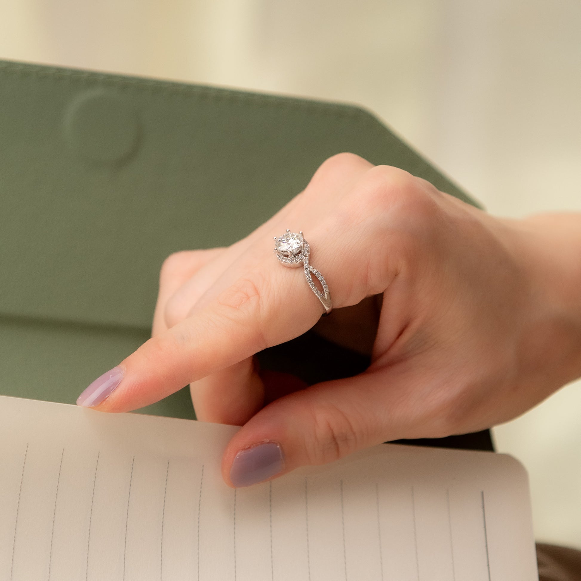 Hand wearing a silver ring with a diamond, resting on a notebook.