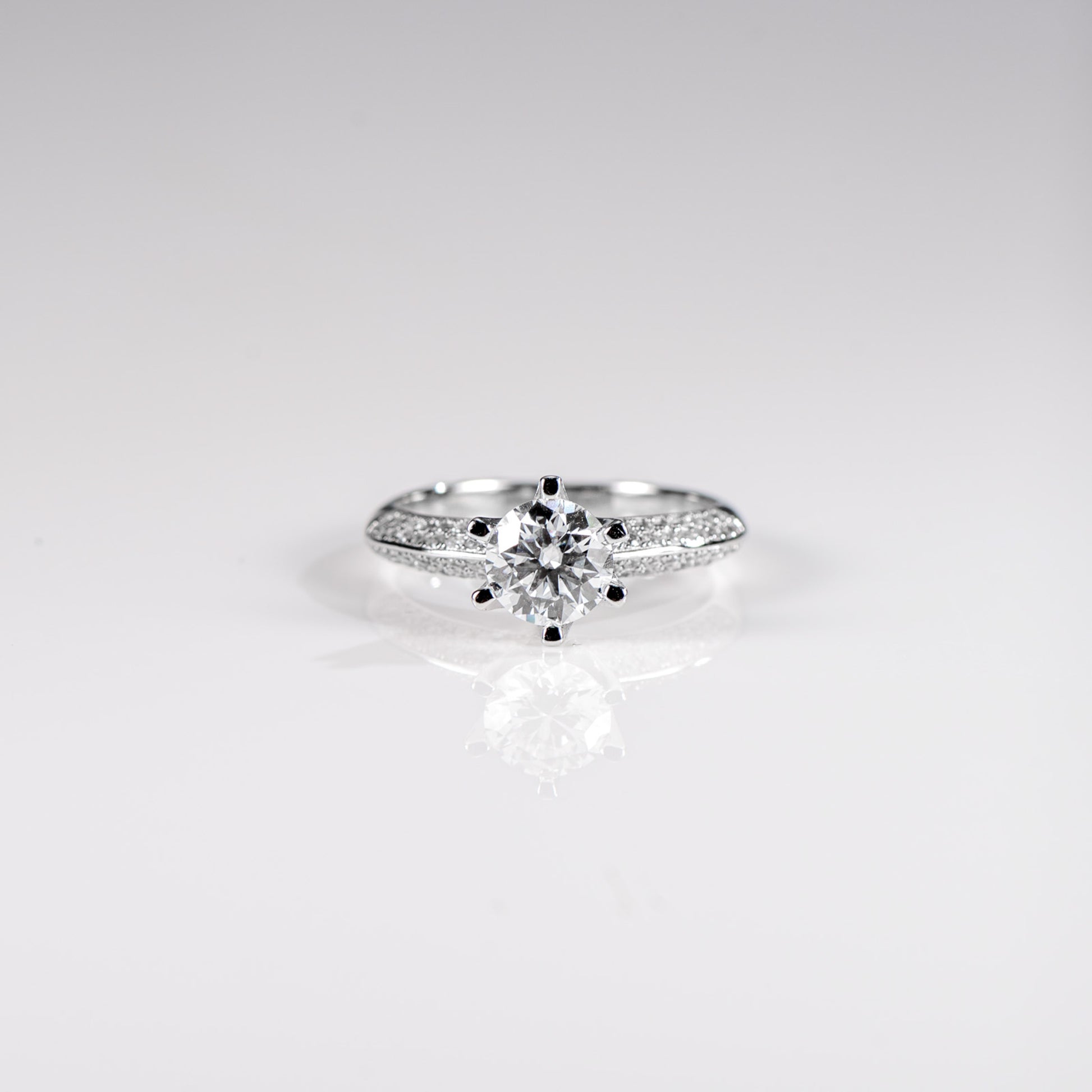Silver ring with a central diamond and smaller stones on a light gray background