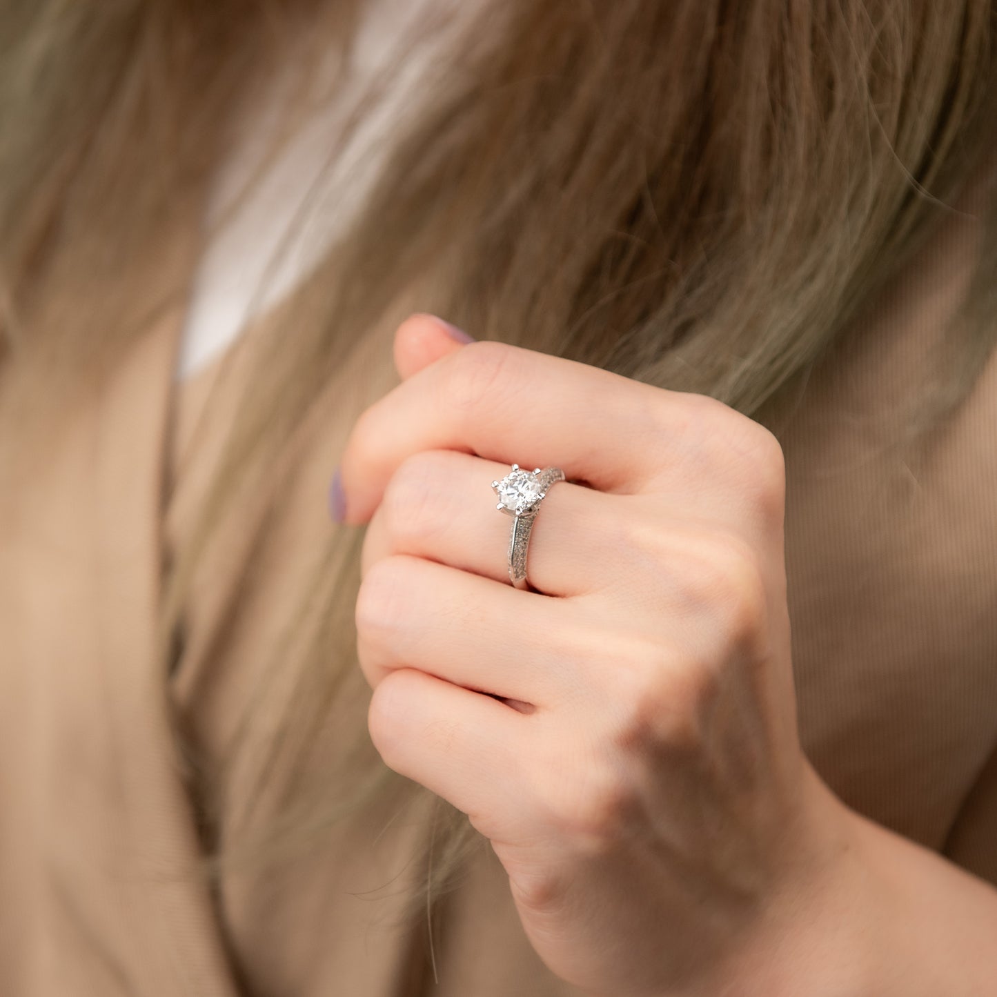 Close-up of a hand wearing a diamond ring with blurred hair in the background