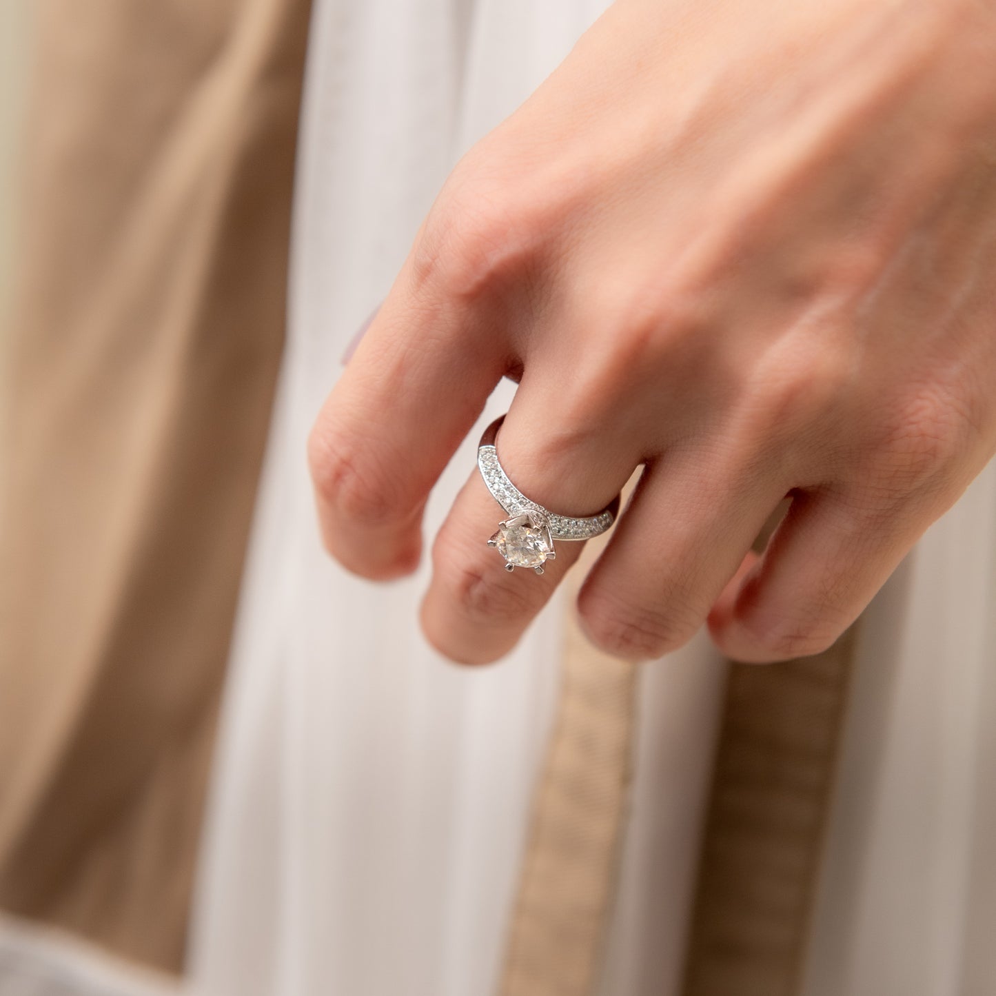 Close-up of a hand wearing a silver ring with a diamond on a neutral background