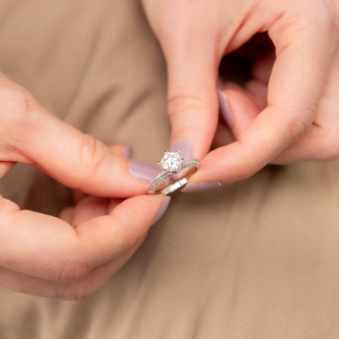 Close-up of hands holding a diamond ring against a beige background